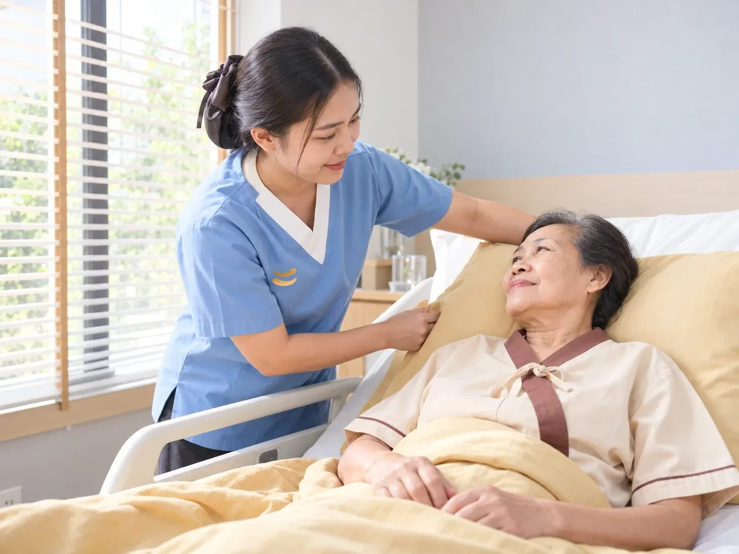 ผู้ดูแลชุดสีฟ้าจัดหมอนรองให้หญิงสูงอายุที่นอนติดเตียงในห้องพัก ศูนย์ฟื้นฟูคิน KIN ผู้ดูแลชุดสีฟ้าจัดหมอนรองให้หญิงสูงอายุที่นอนติดเตียงในห้องพัก ศูนย์ฟื้นฟูคิน KIN