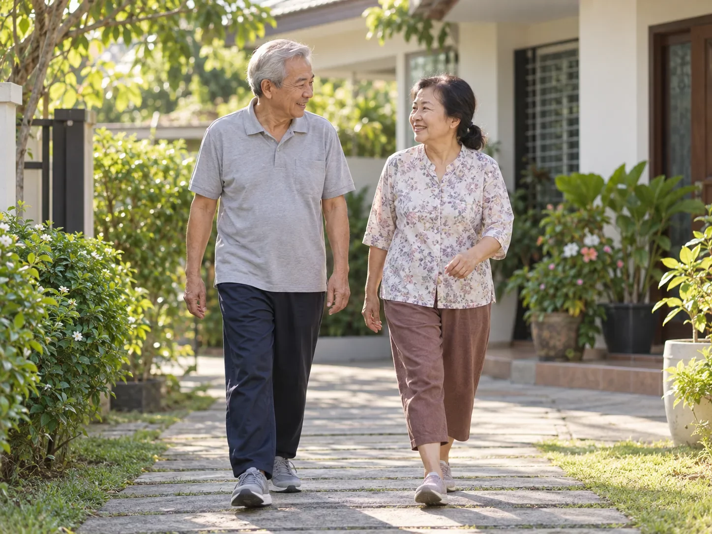 คู่สามีภรรยาสูงอายุเดินออกกำลังกายช้า ๆ ด้วยกันบนทางเดินในสวนหน้าบ้านตอนเช้า ศูนย์ฟื้นฟูคิน KIN